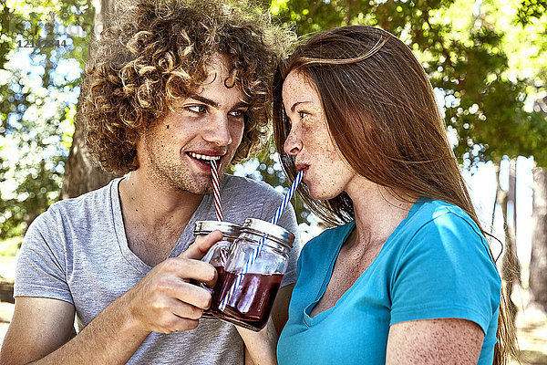 Lächelndes junges Paar bei einem Drink im Wald