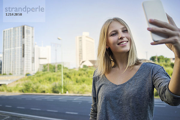 Porträt einer lächelnden jungen Frau  die sich selbst mit dem Smartphone fotografiert.