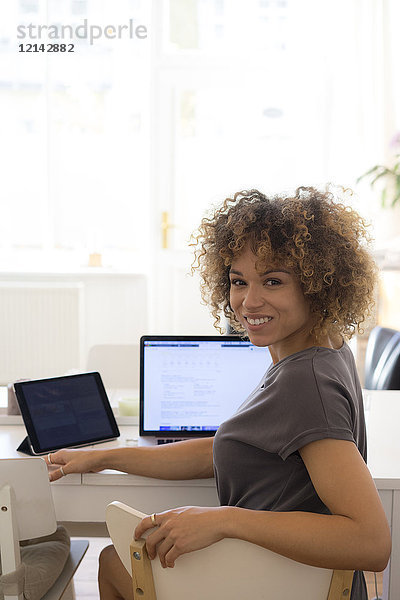 Porträt einer lächelnden jungen Frau zu Hause mit Laptop und Tablett
