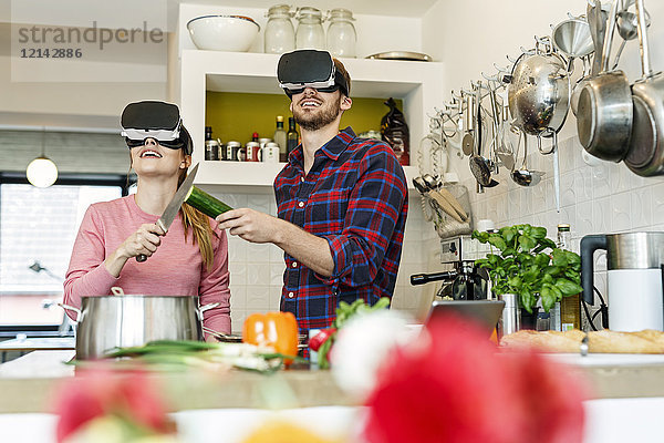 Glückliches junges Paar mit VR-Brille beim gemeinsamen Kochen in der Küche