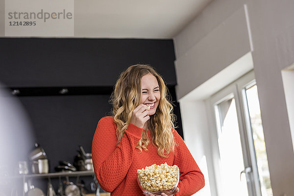 Porträt einer kichernden jungen Frau mit einer Schale Popcorn in der Küche