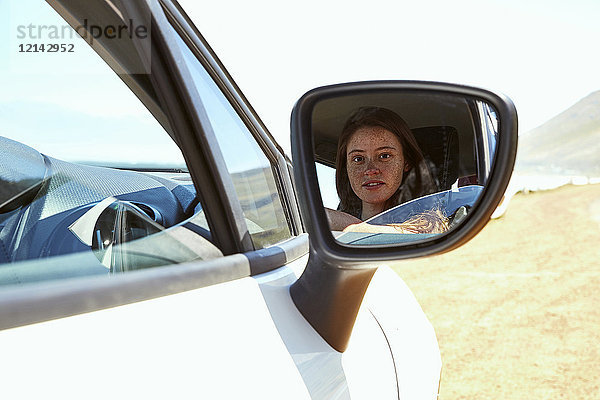 Spiegelung einer jungen Frau im Außenspiegel eines Autos