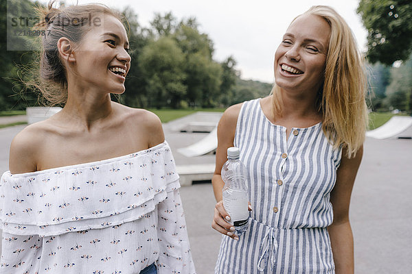 Zwei lachende junge Frauen mit einer Flasche Wasser im Freien.