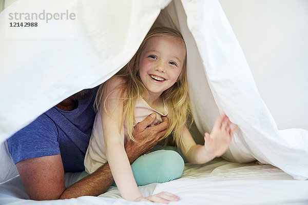 Glückliches Mädchen mit Vater im Bett unter der Decke