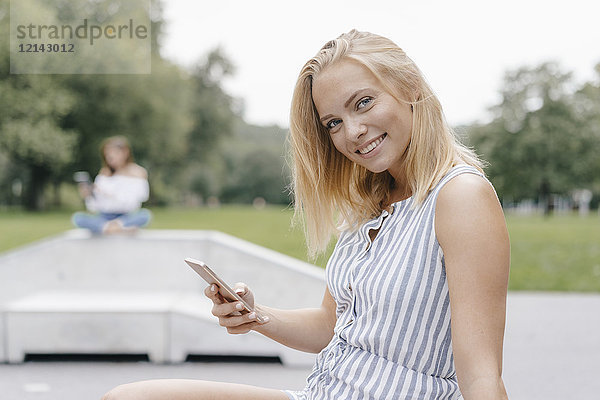 Porträt einer lächelnden jungen Frau mit Handy im Skatepark