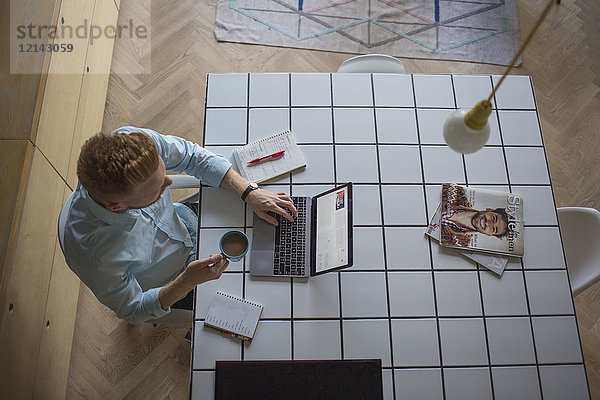 Freiberuflicher Geschäftsmann mit Kaffeetasse  der zu Hause an seinem Laptop arbeitet.