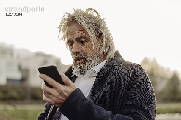 Seriöser älterer Mann mit Handy im Freien