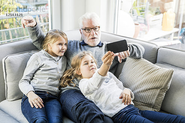 Zwei Mädchen und Großvater auf dem Sofa  die einen Selfie nehmen.