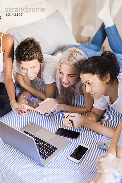 Glückliche weibliche Freunde teilen Laptop im Schlafzimmer