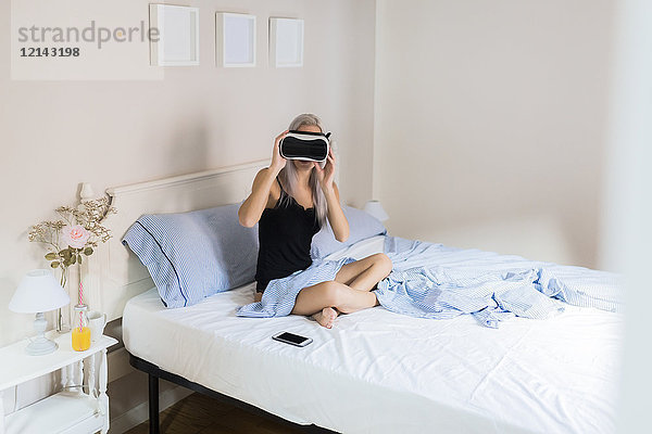 Junge Frau im Bett sitzend mit VR-Brille