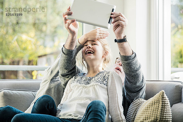 Zwei glückliche Mädchen und Großvater auf dem Sofa  die einen Selfie mit Tablette nehmen.
