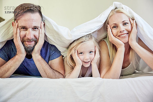 Porträt der glücklichen Familie unter der Decke im Bett