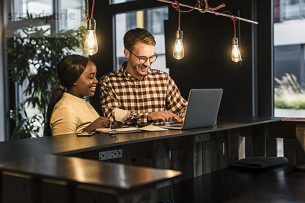 Lächelnde Kollegen arbeiten am Laptop am Tresen