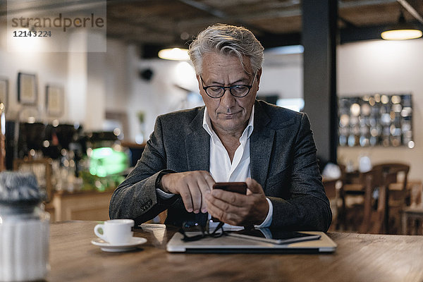 Senior Geschäftsmann sitzt im Café und überprüft Nachrichten auf dem Smartphone.