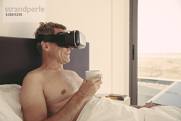 Mann mit VR-Brille im Bett mit Kaffeetasse