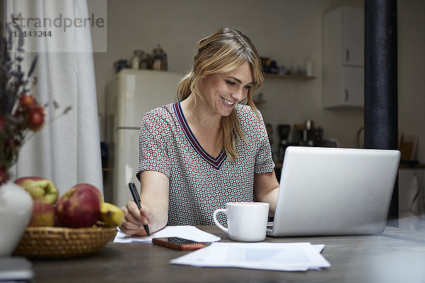 Porträt einer lachenden Frau bei der Arbeit am Laptop zu Hause