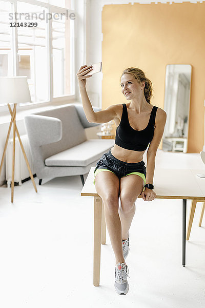 Lächelnde junge Frau in Sportbekleidung mit einem Selfie