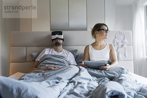 Paar im Bett zu Hause mit Tablette und VR-Brille