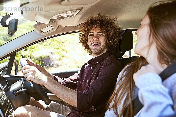 Lachender junger Mann  der Auto fährt und seine Freundin ansieht