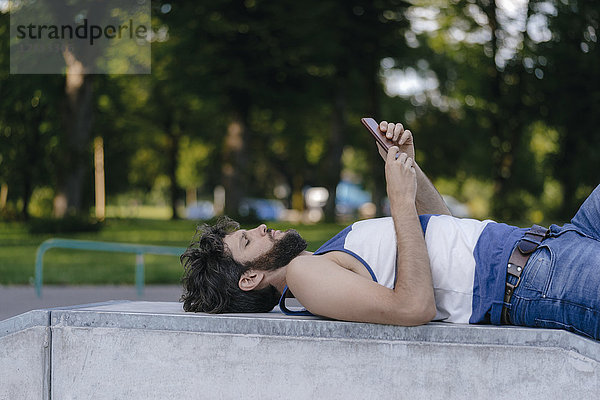 Mann mit Handy im Skatepark liegend