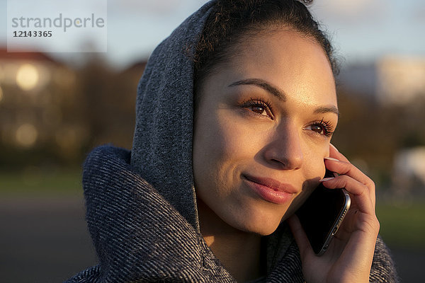 Porträt einer lächelnden jungen Frau auf dem Handy im Freien