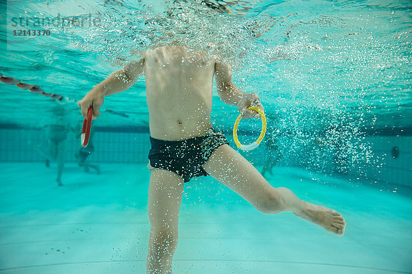 Junge mit zwei Tauchringen unter Wasser im Schwimmbad