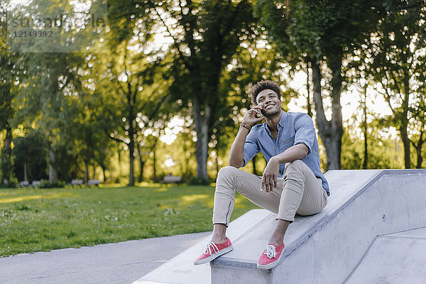 Lächelnder junger Mann am Handy sitzend im Skatepark