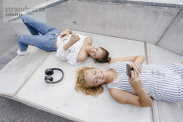Zwei glückliche junge Frauen mit Handy und Kopfhörer im Skatepark