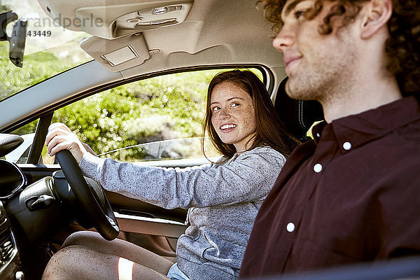 Lächelnde junge Frau fährt Auto und schaut ihren Freund an.