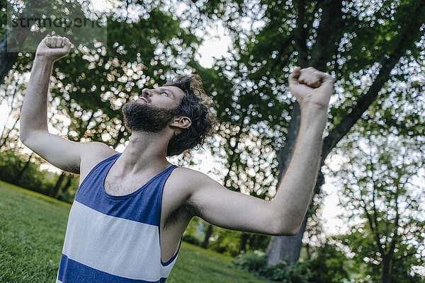 Ein Mann  der seine Arme in einem Park hebt.