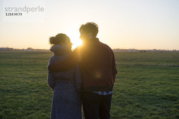 Junges Paar  das bei Sonnenuntergang auf einer Wiese spazieren geht.