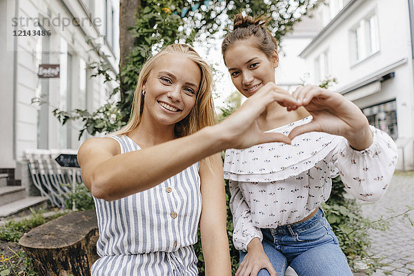 Zwei lächelnde junge Frauen  die mit ihren Händen das Herz in der Stadt formen.