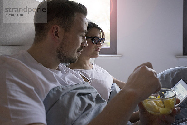 Paar im Bett zu Hause mit Snack und Tablette
