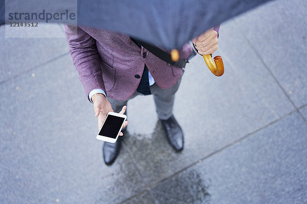 Geschäftsmann unter dem Schirm stehendes Handy  Teilansicht