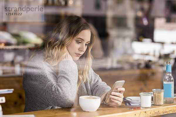 Porträt einer traurigen jungen Frau in einem Coffee-Shop mit Blick auf das Handy