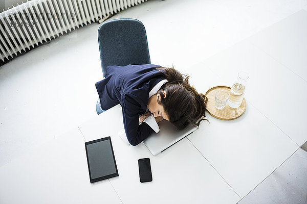 Überarbeitete Geschäftsfrau schläft auf Laptop im Büro  Draufsicht