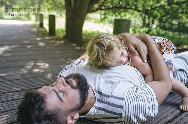 Kleines Mädchen  das seinen Vater umarmt und auf einem Holzsteg auf dem Land liegt.