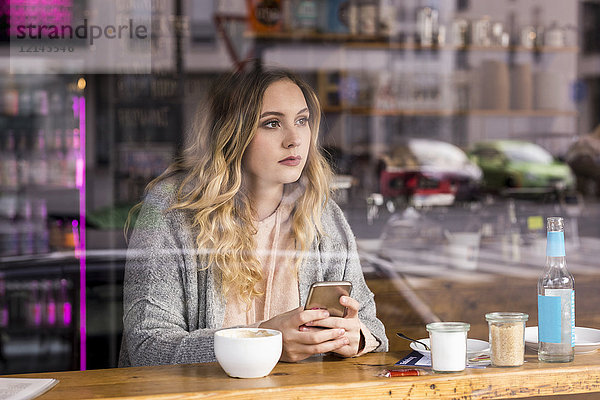 Porträt einer nachdenklichen jungen Frau in einem Café mit Blick durchs Fenster