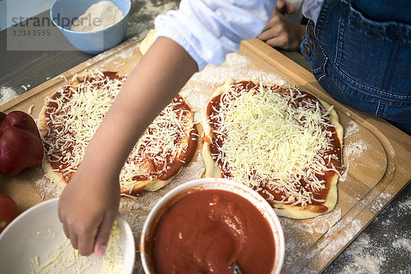 Mädchen in der Küche lernen  wie man Pizza backt  Käse bestreut