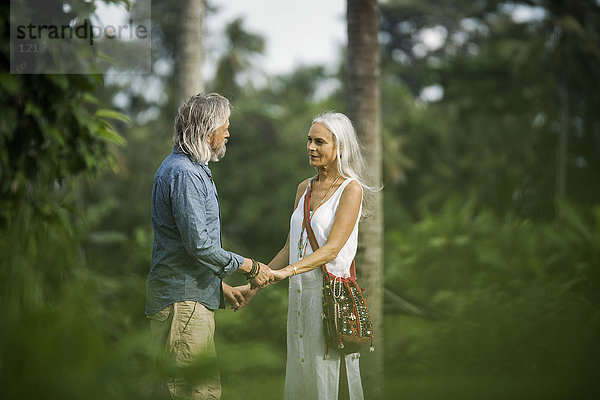 Liebevolles Seniorenpaar hält sich in tropischer Landschaft mit Palmen an den Händen