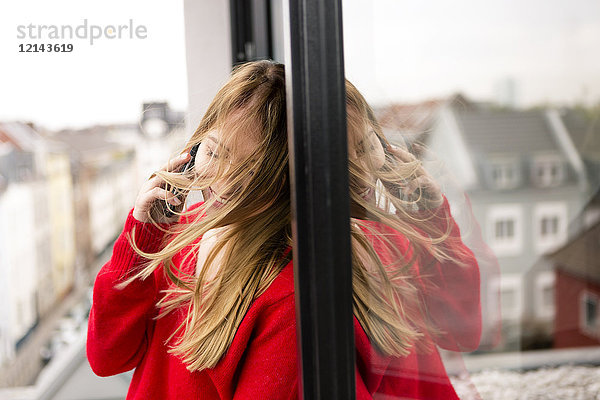 Lächelnde junge Frau am Fenster in der Stadtwohnung am Handy