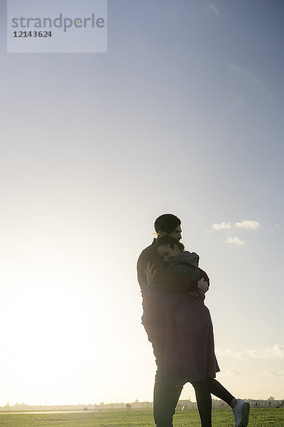 Zärtliches junges Paar  das sich bei Sonnenuntergang auf einer Wiese umarmt.