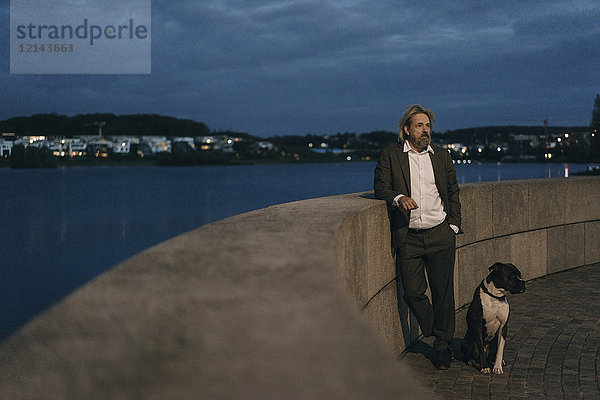 Senior mit Hund am Seeufer stehend am Abend