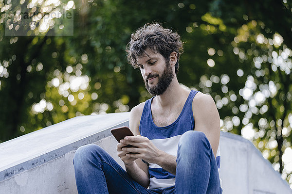 Mann mit Handy im Skatepark sitzend