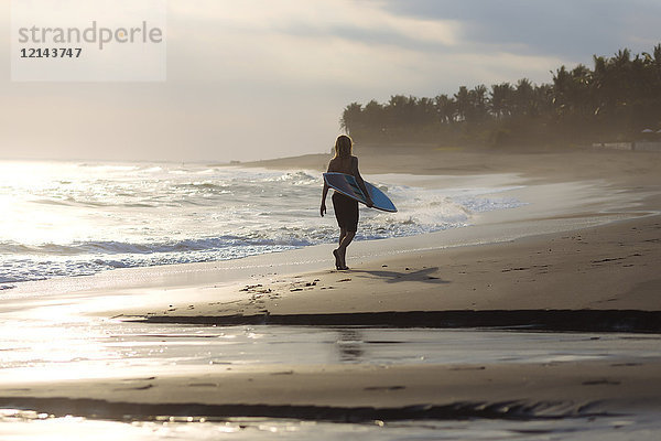 Indonesien  Bali  junger Surfer beim Spaziergang am Strand