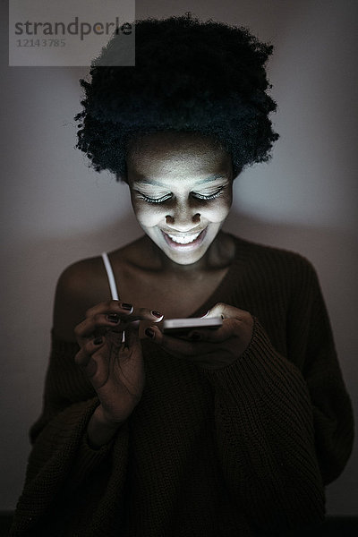 Lächelnde junge Frau mit Handy im Dunkeln