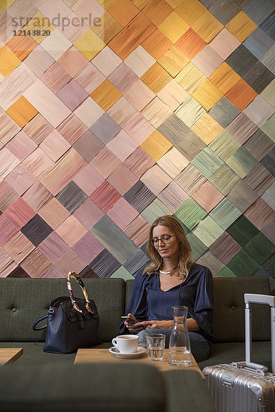 Porträt einer Geschäftsfrau mit Gepäck in einem Café mit Blick aufs Handy