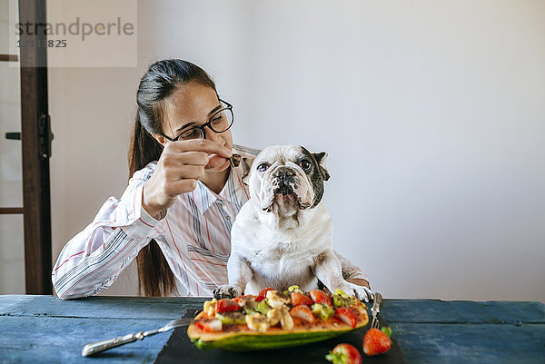 Frau füttert französische Bulldogge am Tisch