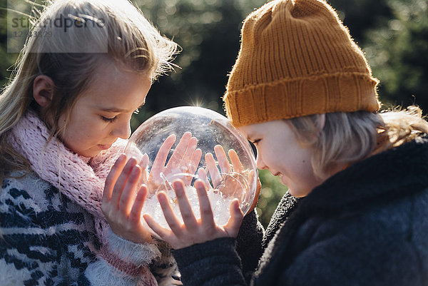 Bruder und Schwester schauen in eine mit Schnee gefüllte Kristallkugel und machen sich einen Wunsch