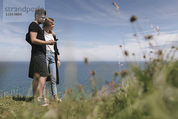 Junges Paar am Meer mit Blick auf das Smartphone